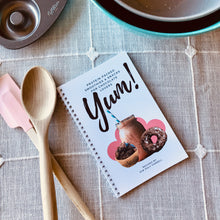 Load image into Gallery viewer, &quot;Yum! Protein-Packed Smoothies &amp; Snacks for Chocolate Lovers&quot; Cookbook on a surface with a tablecloth, mixing spoons, and other baking tools